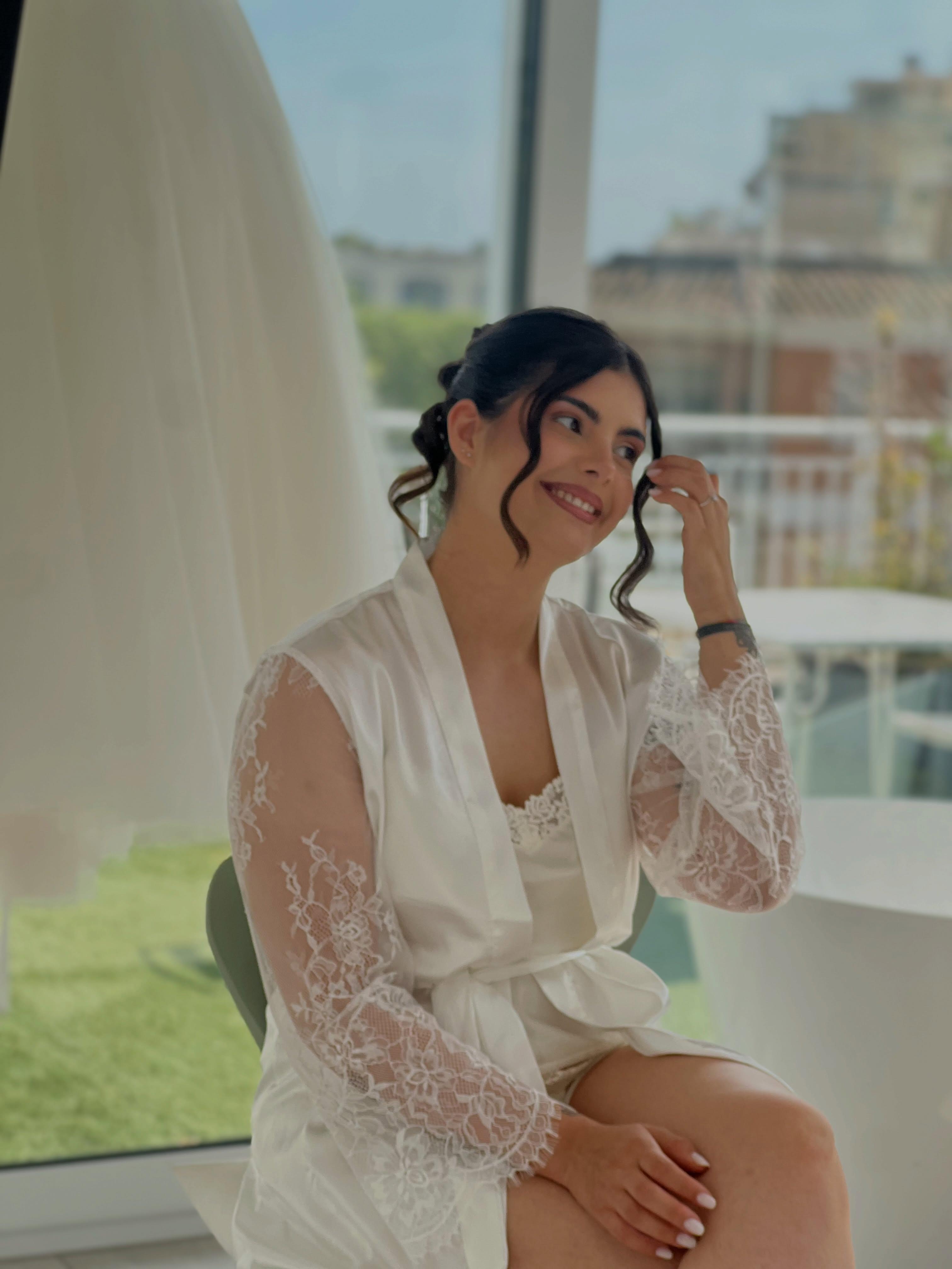 Sposa sorridente durante la preparazione, velo e accappatoio in pizzo